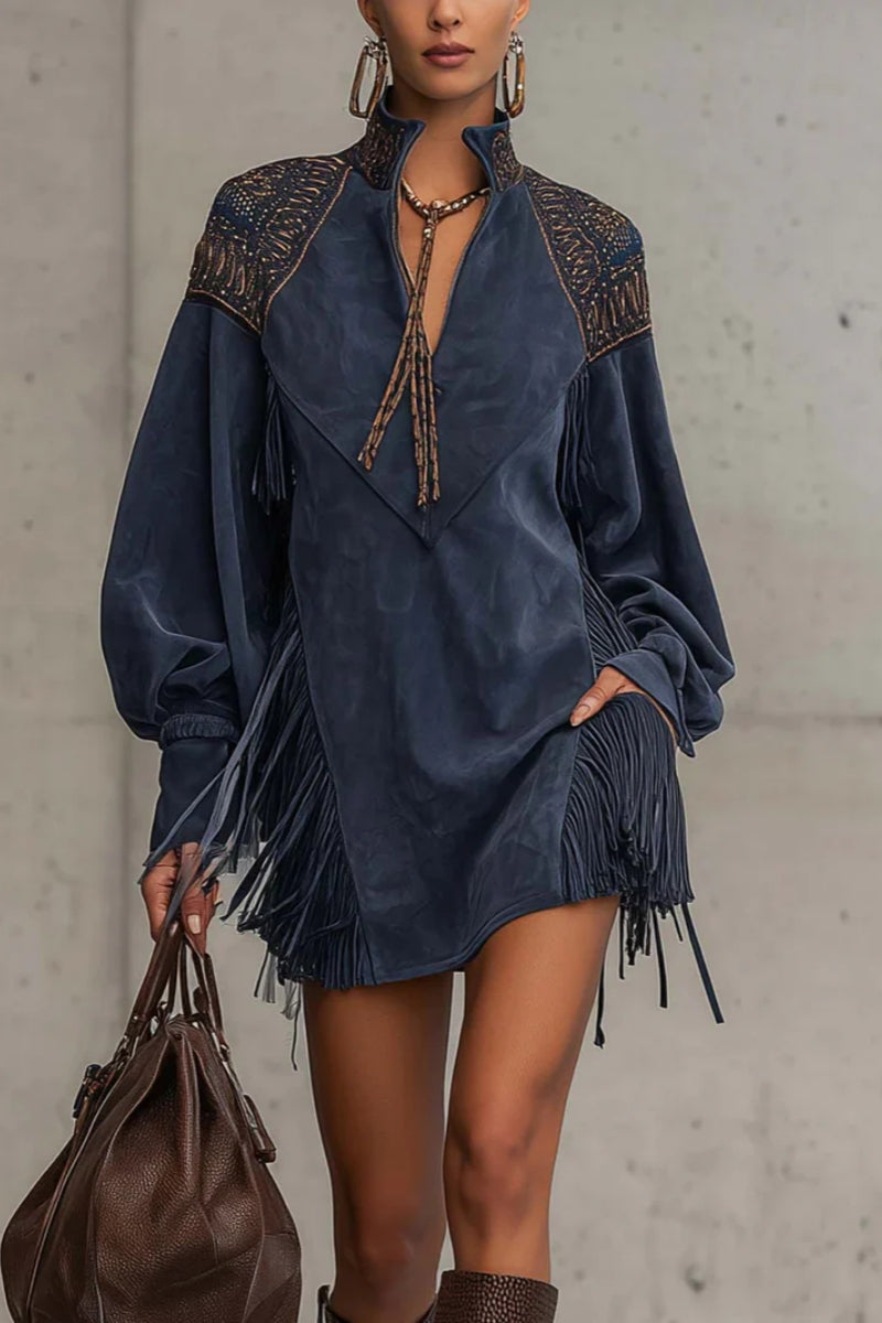 Indige - Model wearing a long-sleeve suede mini dress with deep V-neckline, embroidered shoulder details, and dramatic side fringe, holding a leather handbag.