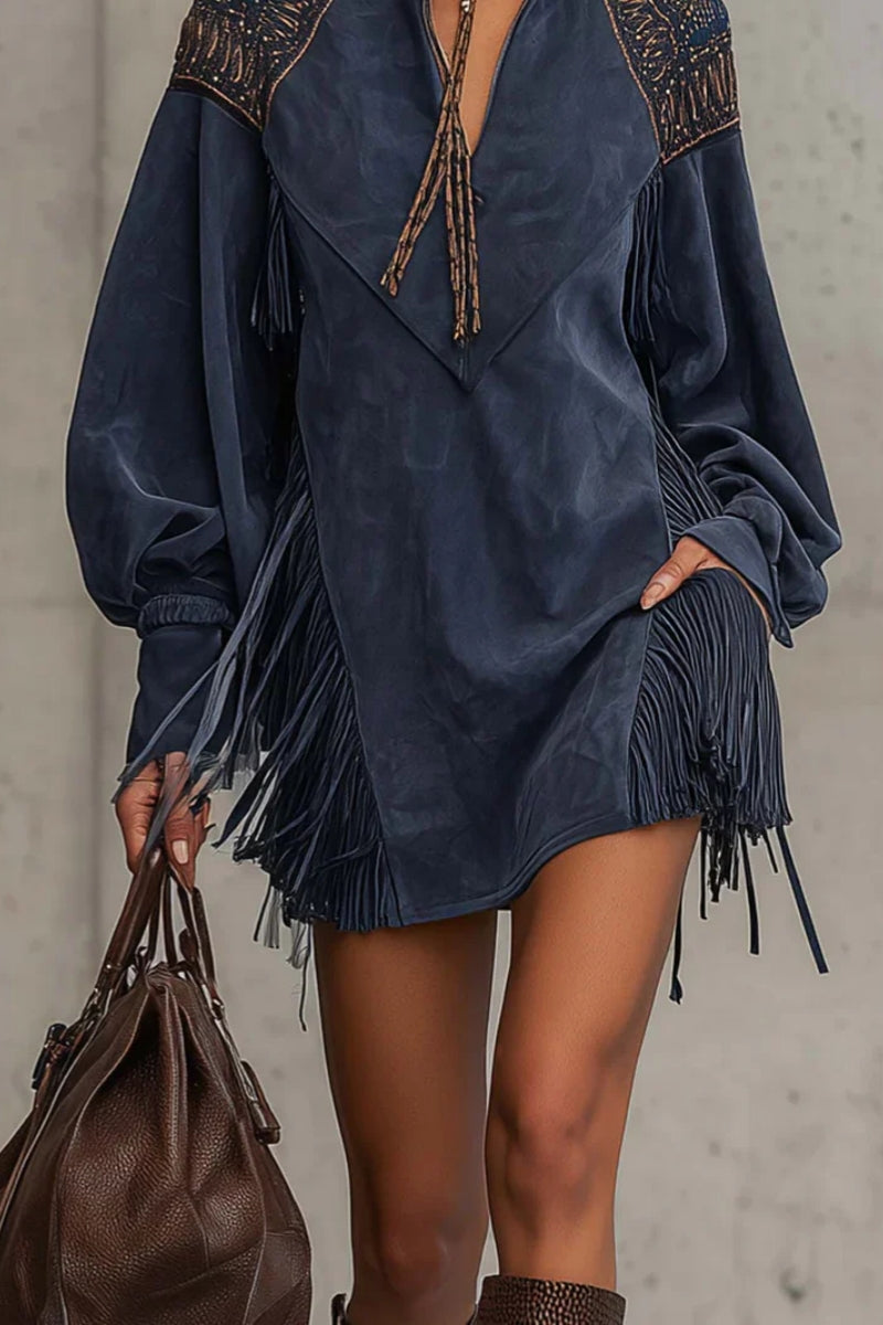 Indige - Model wearing a long-sleeve suede mini dress with deep V-neckline, embroidered shoulder details, and dramatic side fringe, holding a leather handbag.