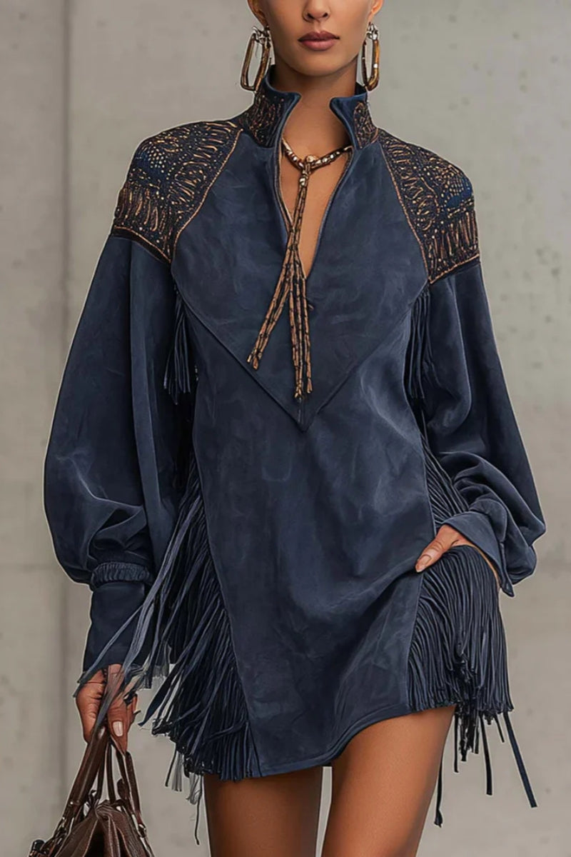 Indige - Model wearing a long-sleeve suede mini dress with deep V-neckline, embroidered shoulder details, and dramatic side fringe, holding a leather handbag.