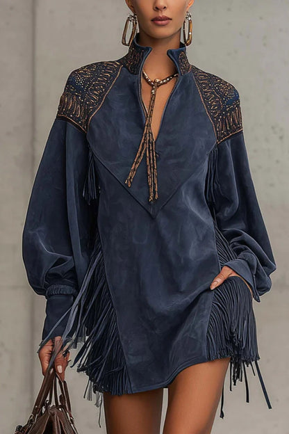 Indige - Model wearing a long-sleeve suede mini dress with deep V-neckline, embroidered shoulder details, and dramatic side fringe, holding a leather handbag.