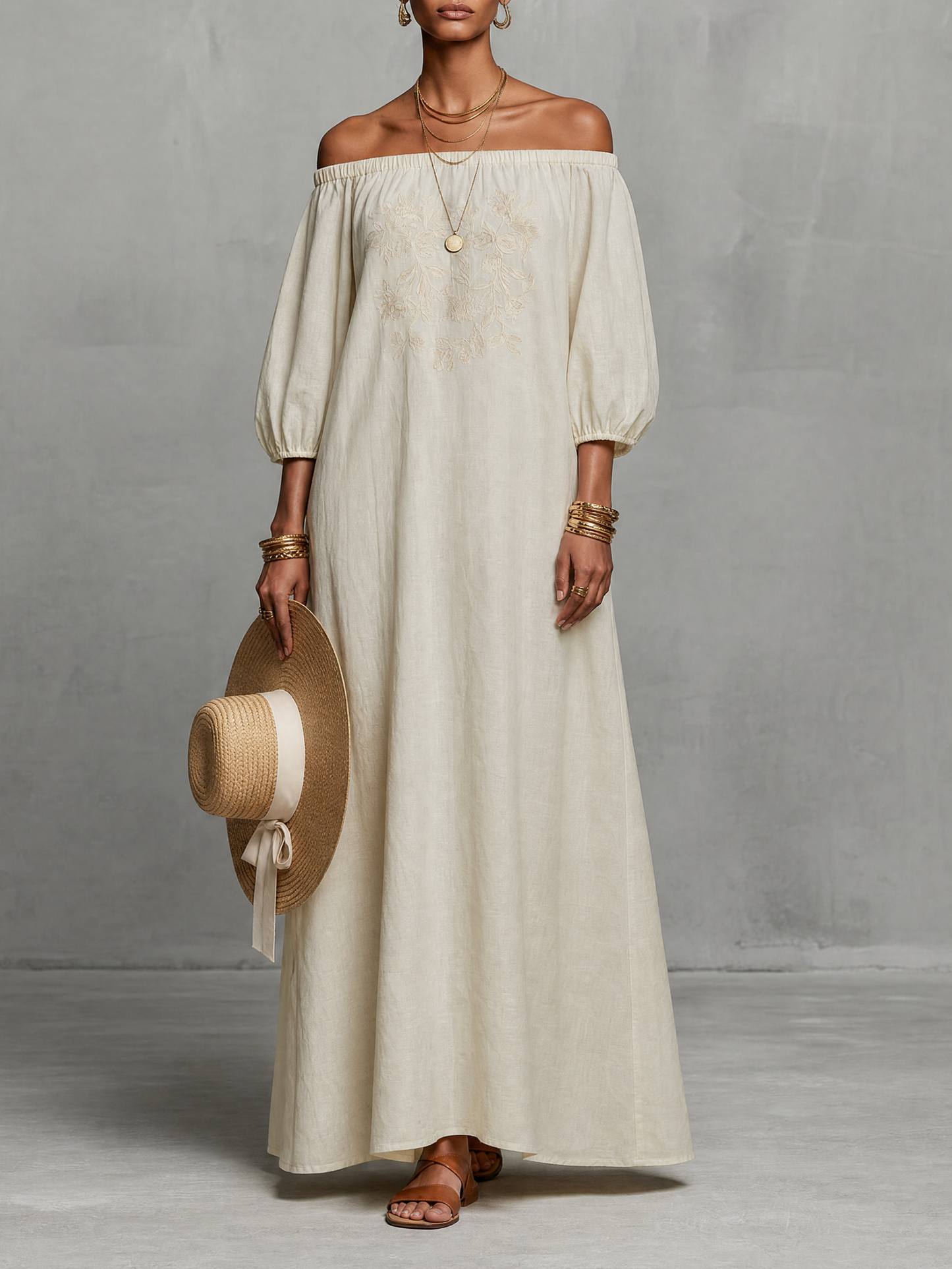 Photo Color - A woman wearing an off-the-shoulder cream linen maxi dress with tonal chest embroidery and puff sleeves, holding a wide-brim straw hat.