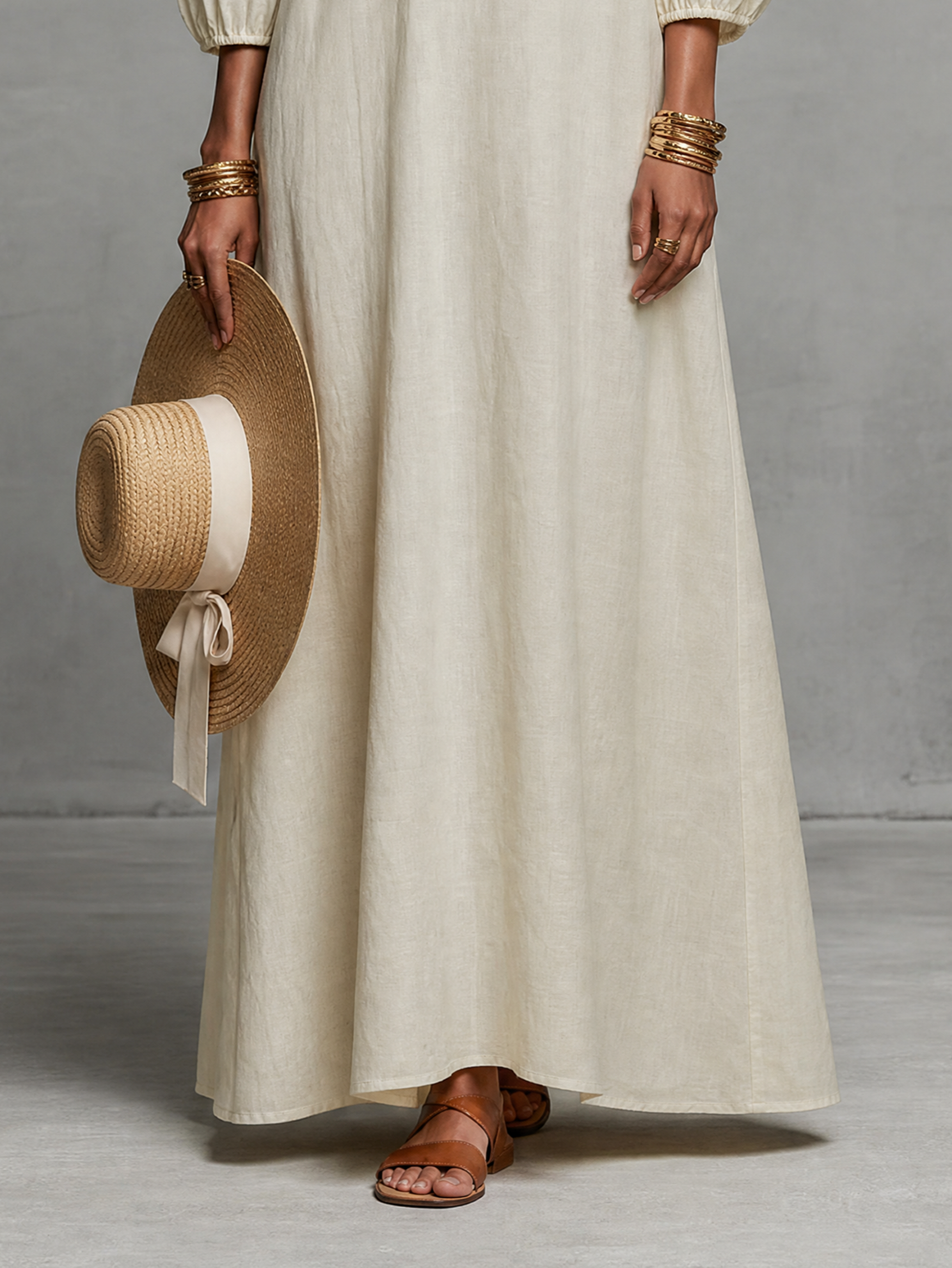 Black - A woman wearing an off-the-shoulder cream linen maxi dress with tonal chest embroidery and puff sleeves, holding a wide-brim straw hat.