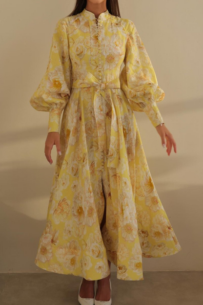 Yellow - A woman wearing a yellow and white floral print maxi dress with long balloon sleeves, a high neckline, button-front detailing, and a self-tie waist.