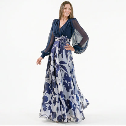 Navy Blue - A woman posing in a floor-length navy and white floral chiffon maxi dress featuring a deep V-neckline, sheer balloon sleeves, and a 3D floral applique at the waist.