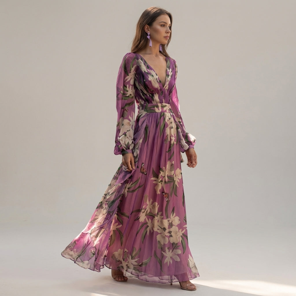 A woman stands wearing a floor-length lavender maxi dress made of sheer floral and butterfly print chiffon, featuring a deep V-neckline, pleated bodice, and long blouson sleeves.
