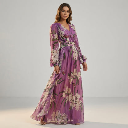 Purple - A woman stands wearing a floor-length lavender maxi dress made of sheer floral and butterfly print chiffon, featuring a deep V-neckline, pleated bodice, and long blouson sleeves.