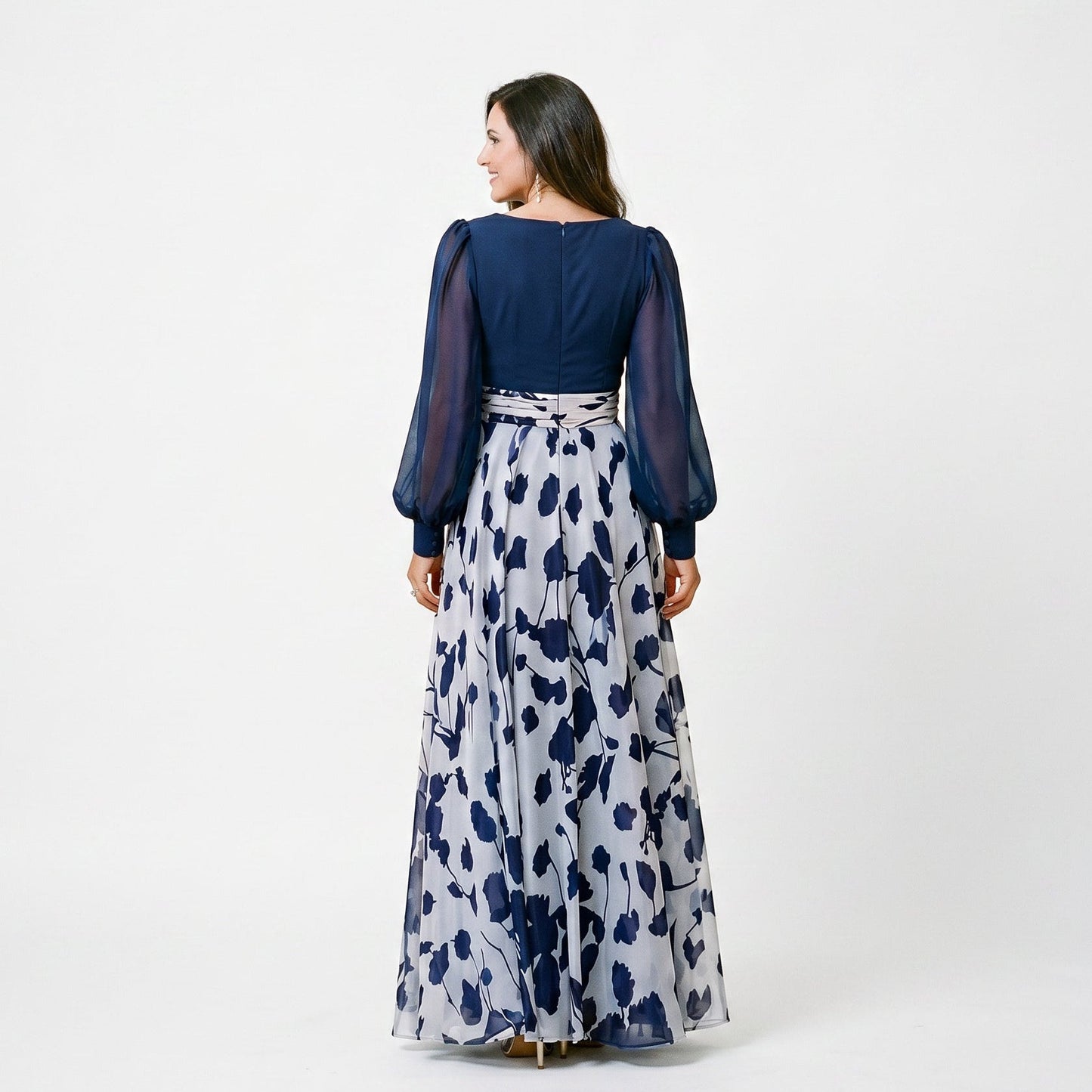 Lilac&Tahiti - A woman posing in a floor-length navy and white floral chiffon maxi dress featuring a deep V-neckline, sheer balloon sleeves, and a 3D floral applique at the waist.