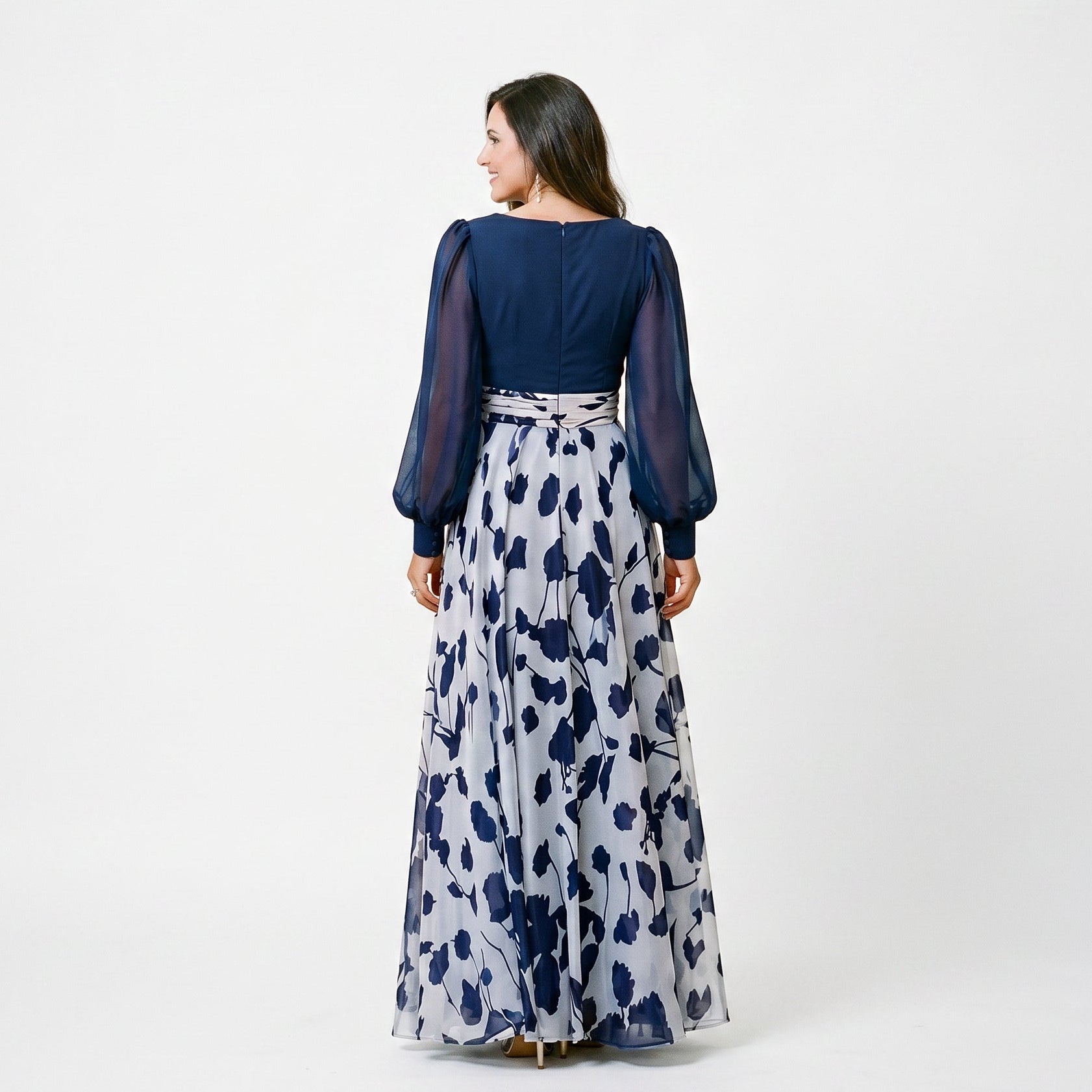 Lilac&Tahiti - A woman posing in a floor-length navy and white floral chiffon maxi dress featuring a deep V-neckline, sheer balloon sleeves, and a 3D floral applique at the waist.