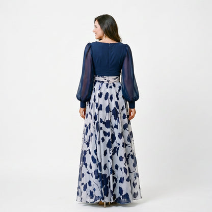 Lilac&Tahiti - A woman posing in a floor-length navy and white floral chiffon maxi dress featuring a deep V-neckline, sheer balloon sleeves, and a 3D floral applique at the waist.