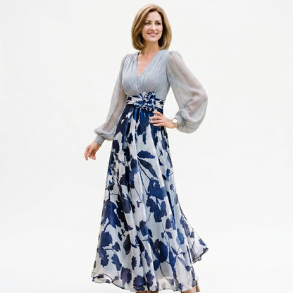 Pale Blue - A woman posing in a floor-length navy and white floral chiffon maxi dress featuring a deep V-neckline, sheer balloon sleeves, and a 3D floral applique at the waist.