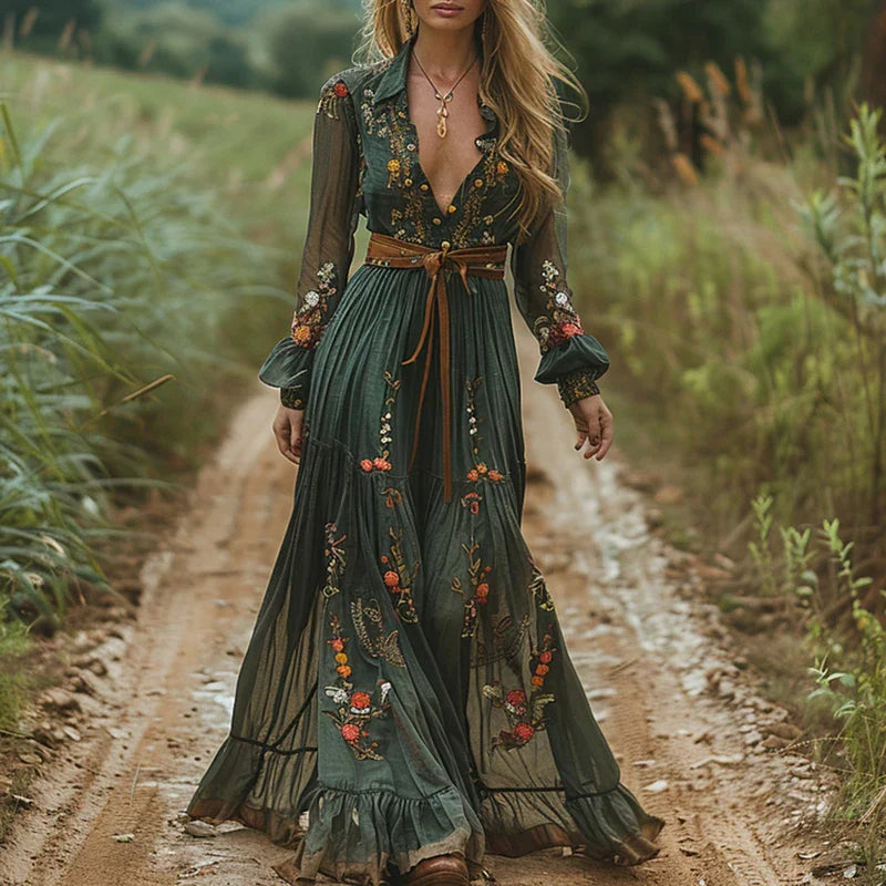 Green (Almost Sold Out) - A woman wearing a long sleeve georgette maxi dress featuring intricate floral embroidery, a button-up front, an adjustable tie waist, and a tiered flowing skirt.
