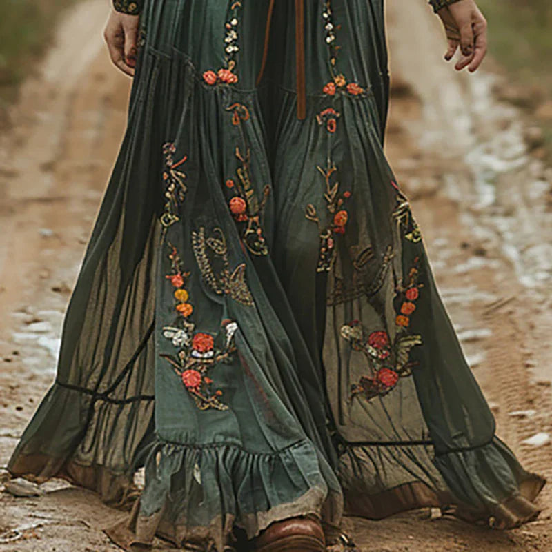 Green (Almost Sold Out) - A woman wearing a long sleeve georgette maxi dress featuring intricate floral embroidery, a button-up front, an adjustable tie waist, and a tiered flowing skirt.
