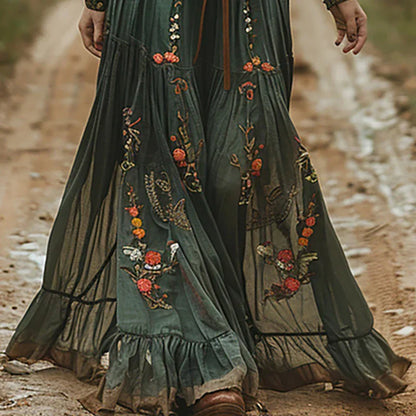 Green (Almost Sold Out) - A woman wearing a long sleeve georgette maxi dress featuring intricate floral embroidery, a button-up front, an adjustable tie waist, and a tiered flowing skirt.
