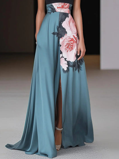 Black - Woman wearing a floor-length maxi dress featuring a solid halter top and a flowing skirt with a large floral placement print and a high front slit.