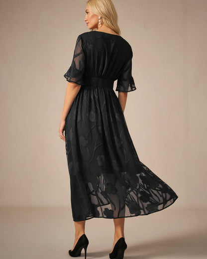 Black - A woman models a black formal midi dress featuring a V-neckline, flutter sleeves, and a textured floral jacquard overlay with a sheer hemline.