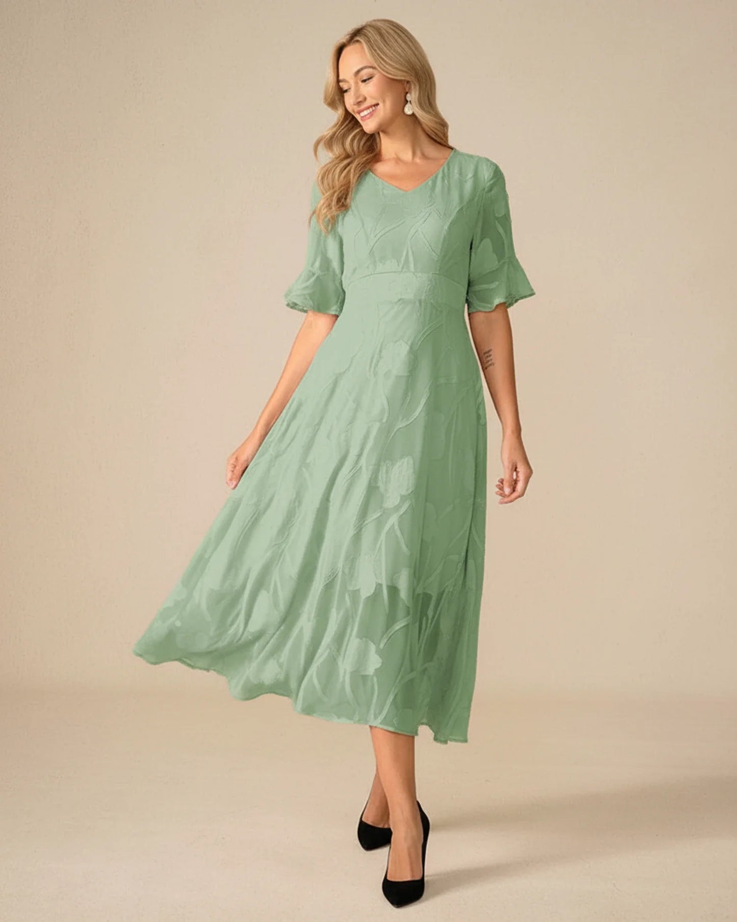 Green - A woman models a black formal midi dress featuring a V-neckline, flutter sleeves, and a textured floral jacquard overlay with a sheer hemline.