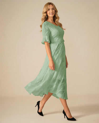 Green - A woman models a black formal midi dress featuring a V-neckline, flutter sleeves, and a textured floral jacquard overlay with a sheer hemline.