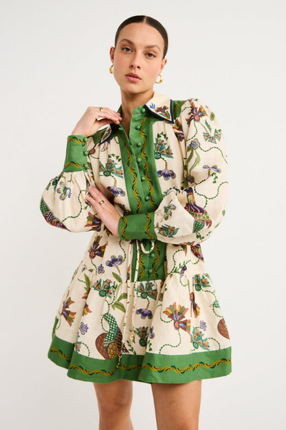 Green - Woman wearing a floral print long-sleeve mini dress with a collared neckline, covered buttons, and a tiered skirt against a plain background.