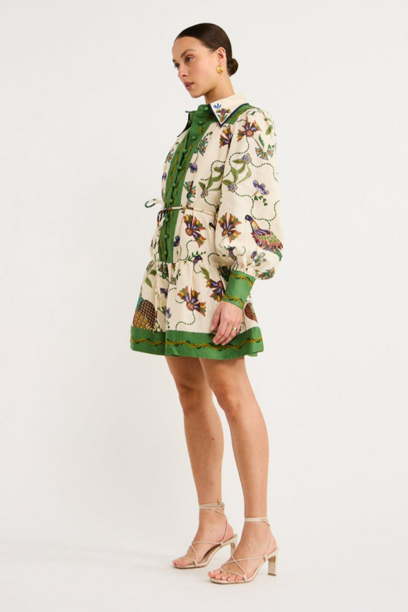 Green - Woman wearing a floral print long-sleeve mini dress with a collared neckline, covered buttons, and a tiered skirt against a plain background.