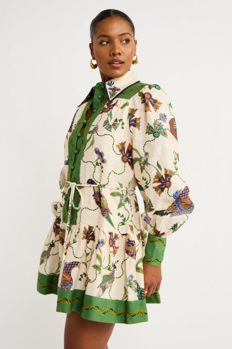 Green - Woman wearing a floral print long-sleeve mini dress with a collared neckline, covered buttons, and a tiered skirt against a plain background.