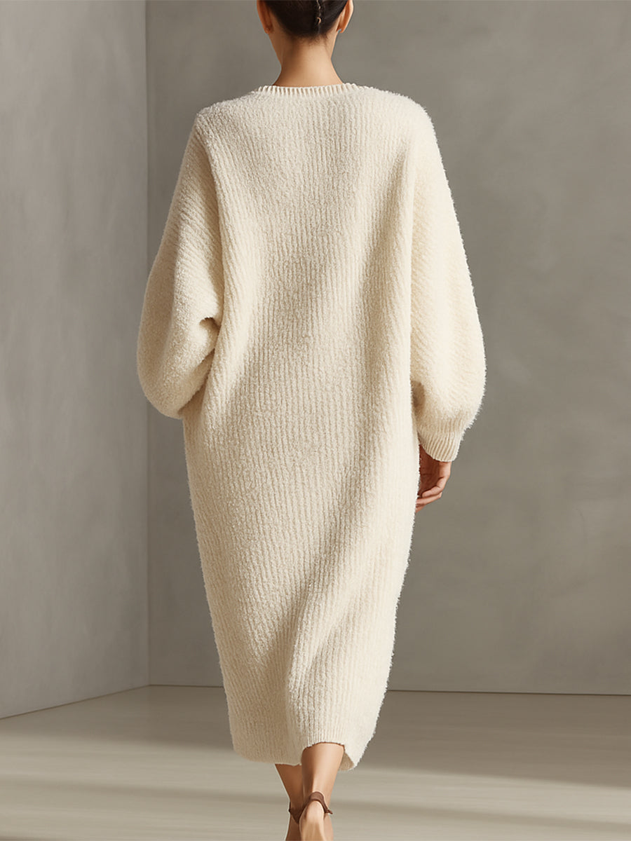 Cream - A woman wearing an oversized, cream-coloured fluffy knit midi dress with a high neckline, long voluminous sleeves, and an asymmetric draped wrap hemline.