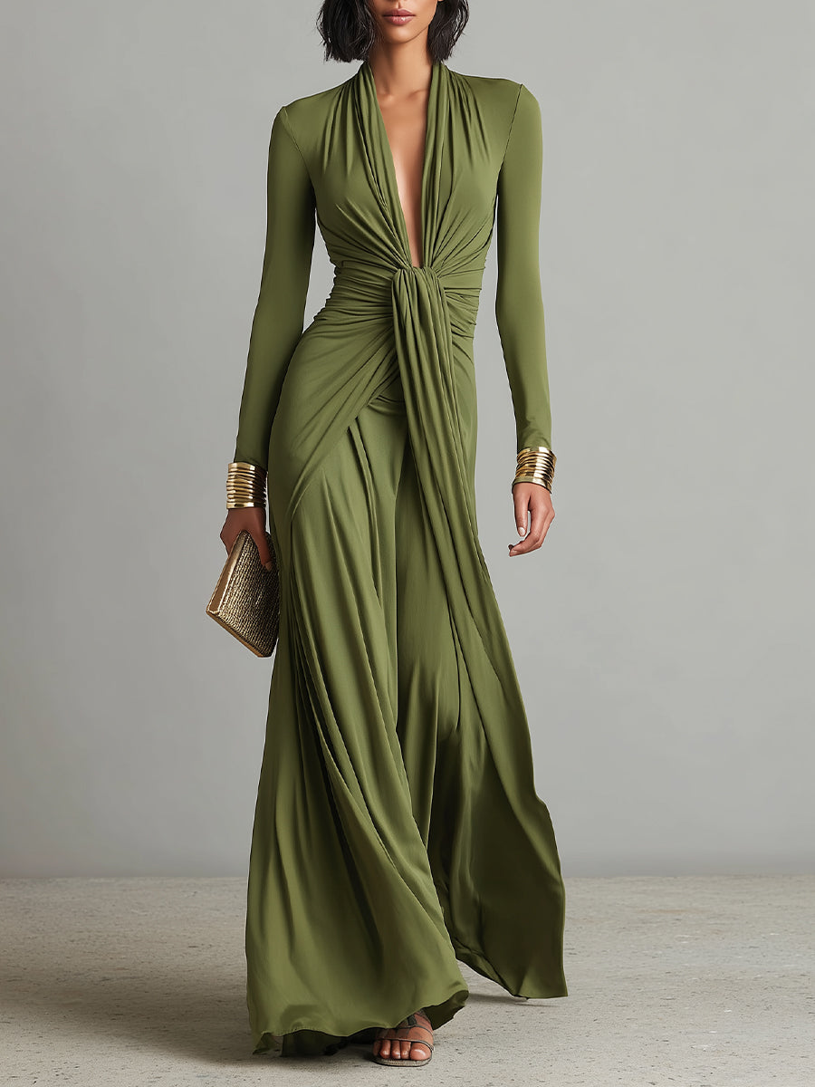 Green - A woman wears an olive green long-sleeve maxi dress crafted from fluid jersey, featuring a deep plunging V-neckline, a central ruched knot at the waist, and a cascading floor-length skirt.