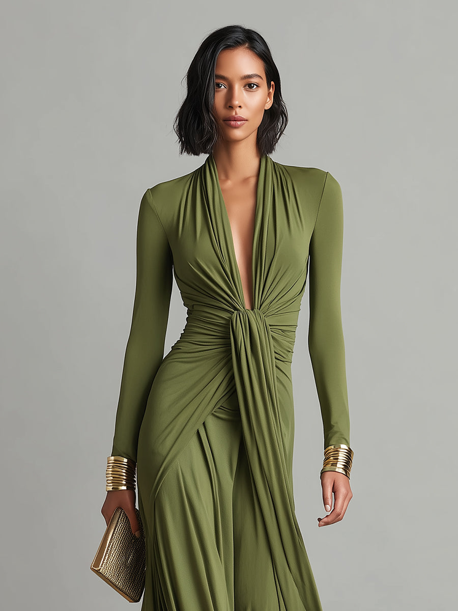 Green - A woman wears an olive green long-sleeve maxi dress crafted from fluid jersey, featuring a deep plunging V-neckline, a central ruched knot at the waist, and a cascading floor-length skirt.