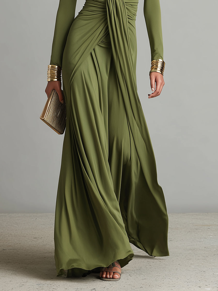 Green - A woman wears an olive green long-sleeve maxi dress crafted from fluid jersey, featuring a deep plunging V-neckline, a central ruched knot at the waist, and a cascading floor-length skirt.
