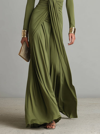 Green - A woman wears an olive green long-sleeve maxi dress crafted from fluid jersey, featuring a deep plunging V-neckline, a central ruched knot at the waist, and a cascading floor-length skirt.