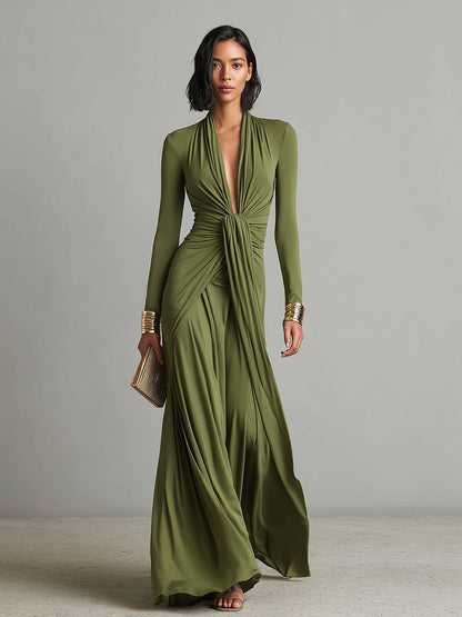 Green - A woman wears an olive green long-sleeve maxi dress crafted from fluid jersey, featuring a deep plunging V-neckline, a central ruched knot at the waist, and a cascading floor-length skirt.