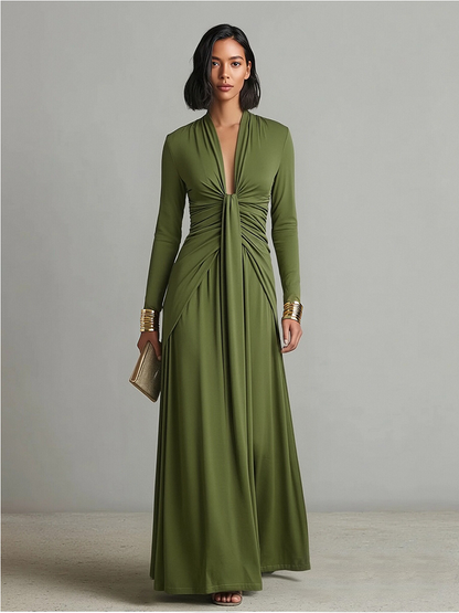 Green - A woman wears an olive green long-sleeve maxi dress crafted from fluid jersey, featuring a deep plunging V-neckline, a central ruched knot at the waist, and a cascading floor-length skirt.