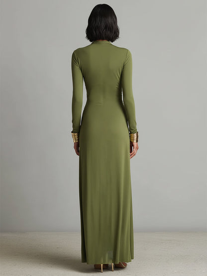 Green - A woman wears an olive green long-sleeve maxi dress crafted from fluid jersey, featuring a deep plunging V-neckline, a central ruched knot at the waist, and a cascading floor-length skirt.