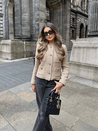 Beige - A woman wearing a beige textured boucle cropped jacket with gold buttons and fringed edges, styled over a light blue ruffled blouse and high-waisted jeans.