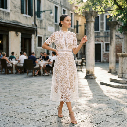 Black - A woman wearing a black geometric lace midi dress with a high neck, short sleeves, and a defined waist, featuring a nude lining and scalloped hem.