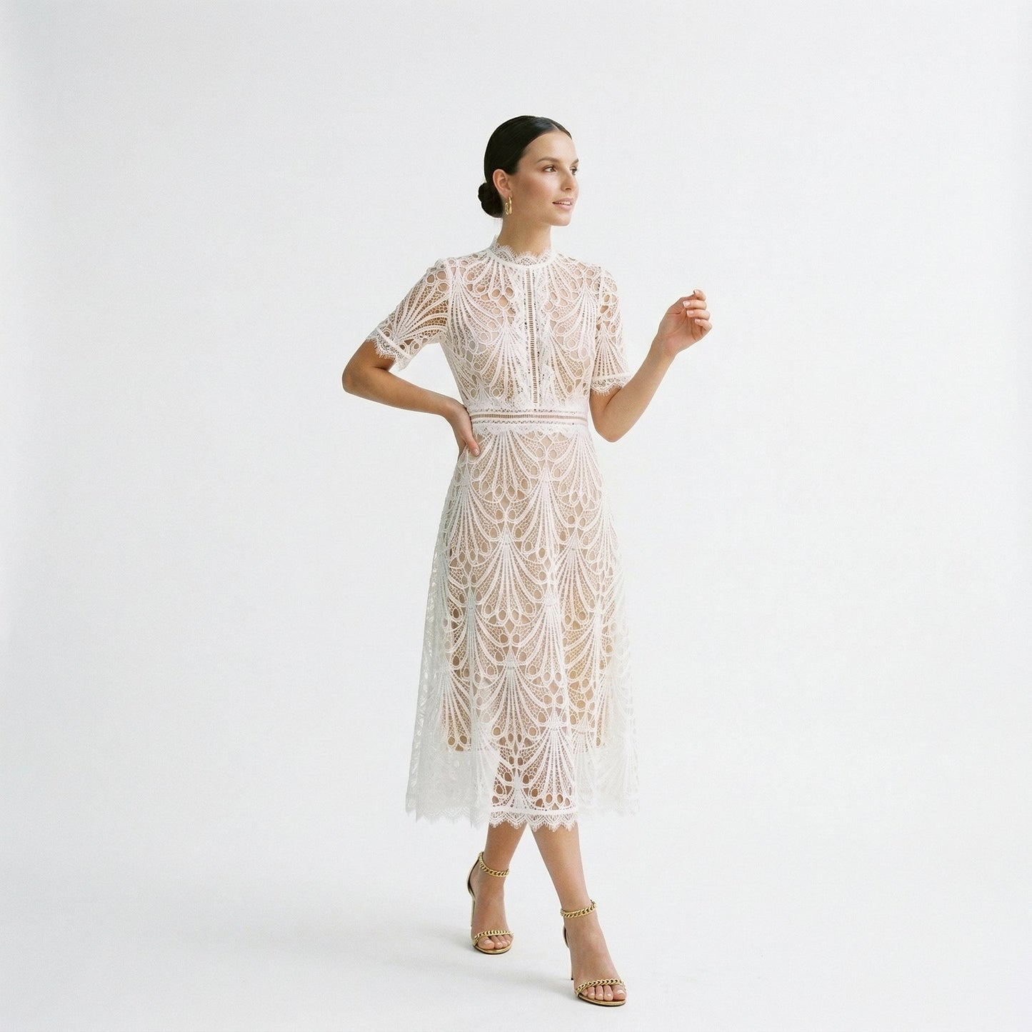 White - A woman wearing a black geometric lace midi dress with a high neck, short sleeves, and a defined waist, featuring a nude lining and scalloped hem.