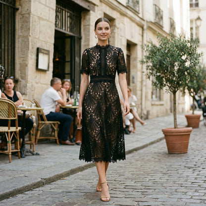 White - A woman wearing a black geometric lace midi dress with a high neck, short sleeves, and a defined waist, featuring a nude lining and scalloped hem.