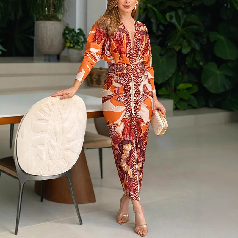 XL - A woman wearing a long-sleeve midi dress featuring a bold, symmetrical graphic print in orange, terracotta, and cream, with a deep plunging V-neckline and a ruched waist.