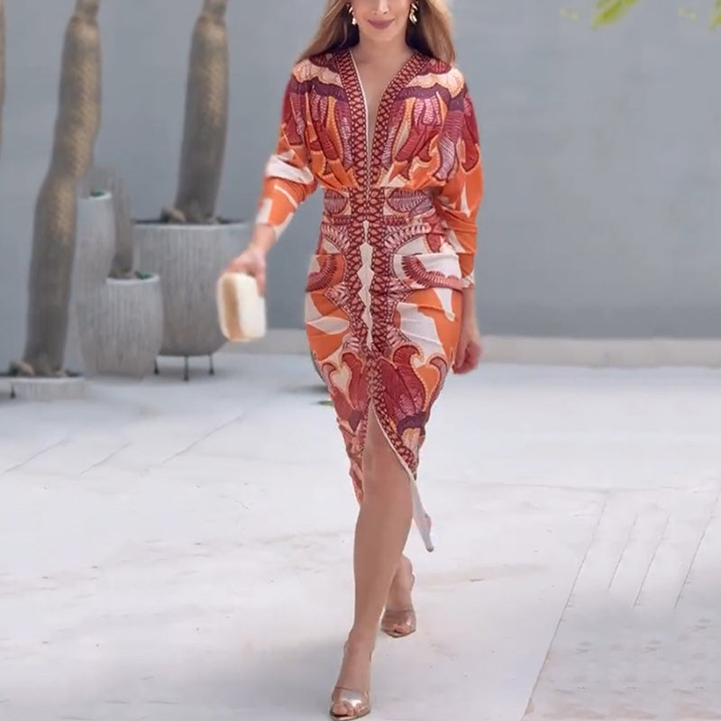XL - A woman wearing a long-sleeve midi dress featuring a bold, symmetrical graphic print in orange, terracotta, and cream, with a deep plunging V-neckline and a ruched waist.