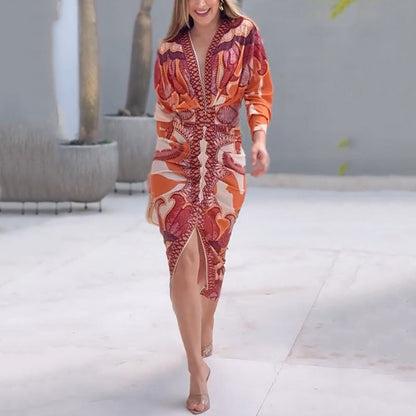 XL - A woman wearing a long-sleeve midi dress featuring a bold, symmetrical graphic print in orange, terracotta, and cream, with a deep plunging V-neckline and a ruched waist.