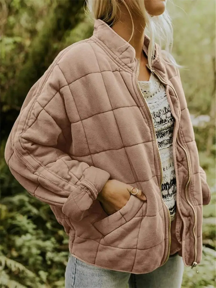 Khaki - A woman wearing a sage green grid-quilted jacket with a high funnel neck and gold-tone zip front, layered over a cream knit sweater and light-wash denim jeans.