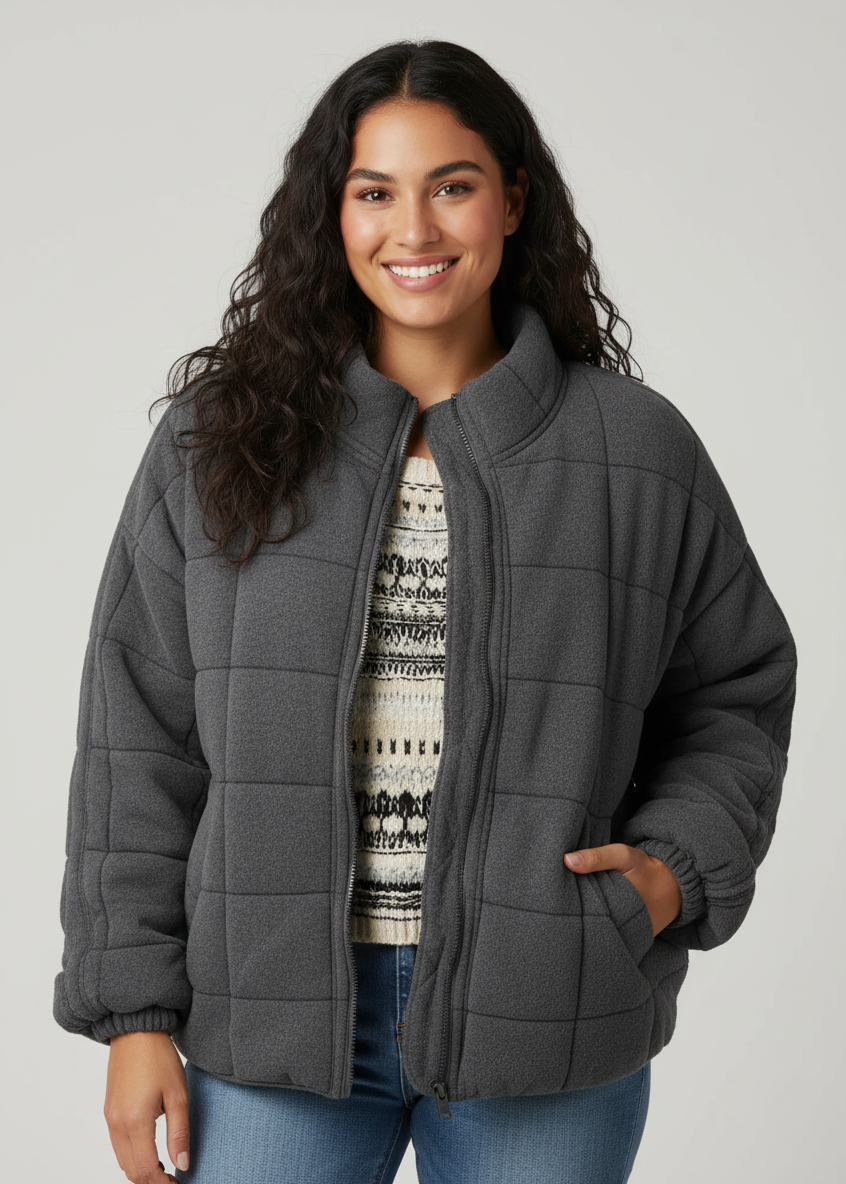 Dark Grey - A woman wearing a sage green grid-quilted jacket with a high funnel neck and gold-tone zip front, layered over a cream knit sweater and light-wash denim jeans.