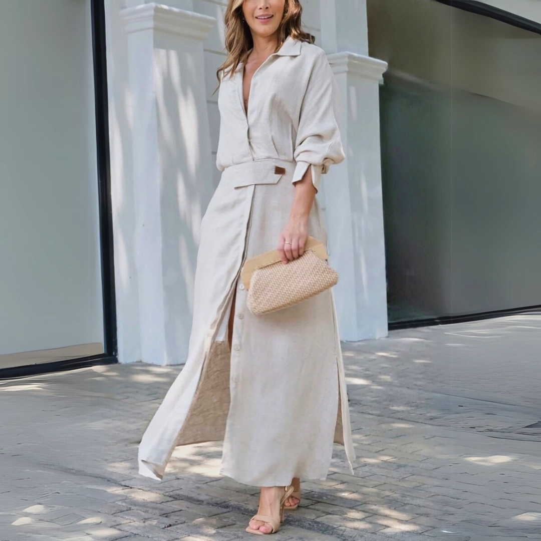 Beige - Woman walking outdoors wearing a long textured linen maxi dress with long sleeves, a collar, button front, and waist belt, carrying a woven clutch.