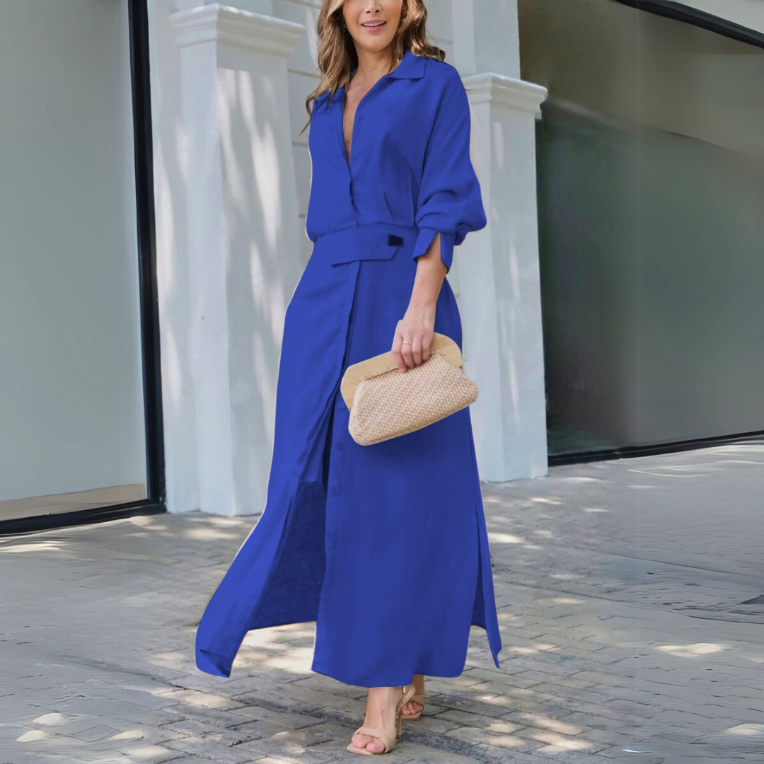 Blue - Woman walking outdoors wearing a long textured linen maxi dress with long sleeves, a collar, button front, and waist belt, carrying a woven clutch.