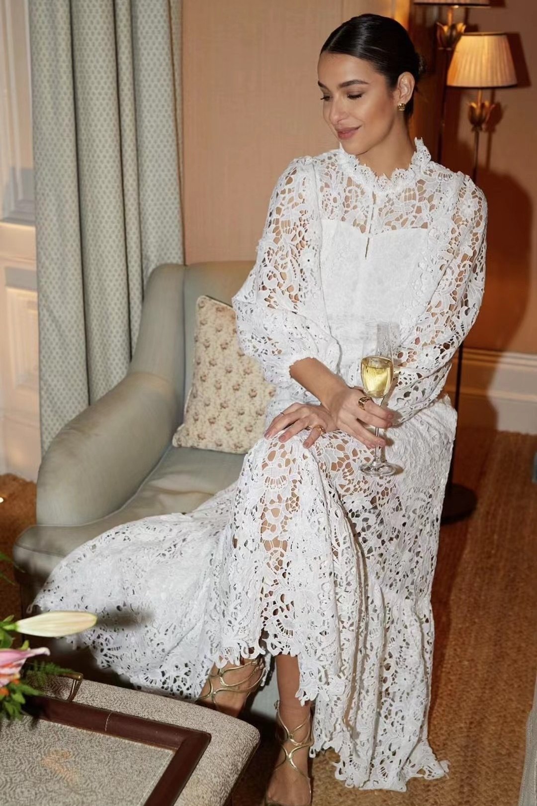 White - A woman models a vibrant green, long-sleeve maxi dress featuring an intricate floral lace overlay, a high neckline, and a tiered skirt, holding a matching green clutch in a greenhouse setting.