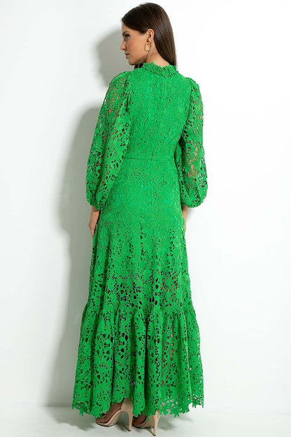 Green - A woman models a vibrant green, long-sleeve maxi dress featuring an intricate floral lace overlay, a high neckline, and a tiered skirt, holding a matching green clutch in a greenhouse setting.