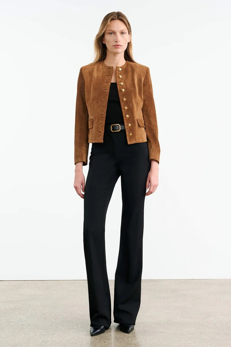 Brown - A woman wearing a tan, collarless suede cropped jacket with gold-tone buttons over a black top and trousers.
