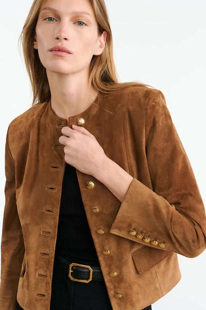 Brown - A woman wearing a tan, collarless suede cropped jacket with gold-tone buttons over a black top and trousers.