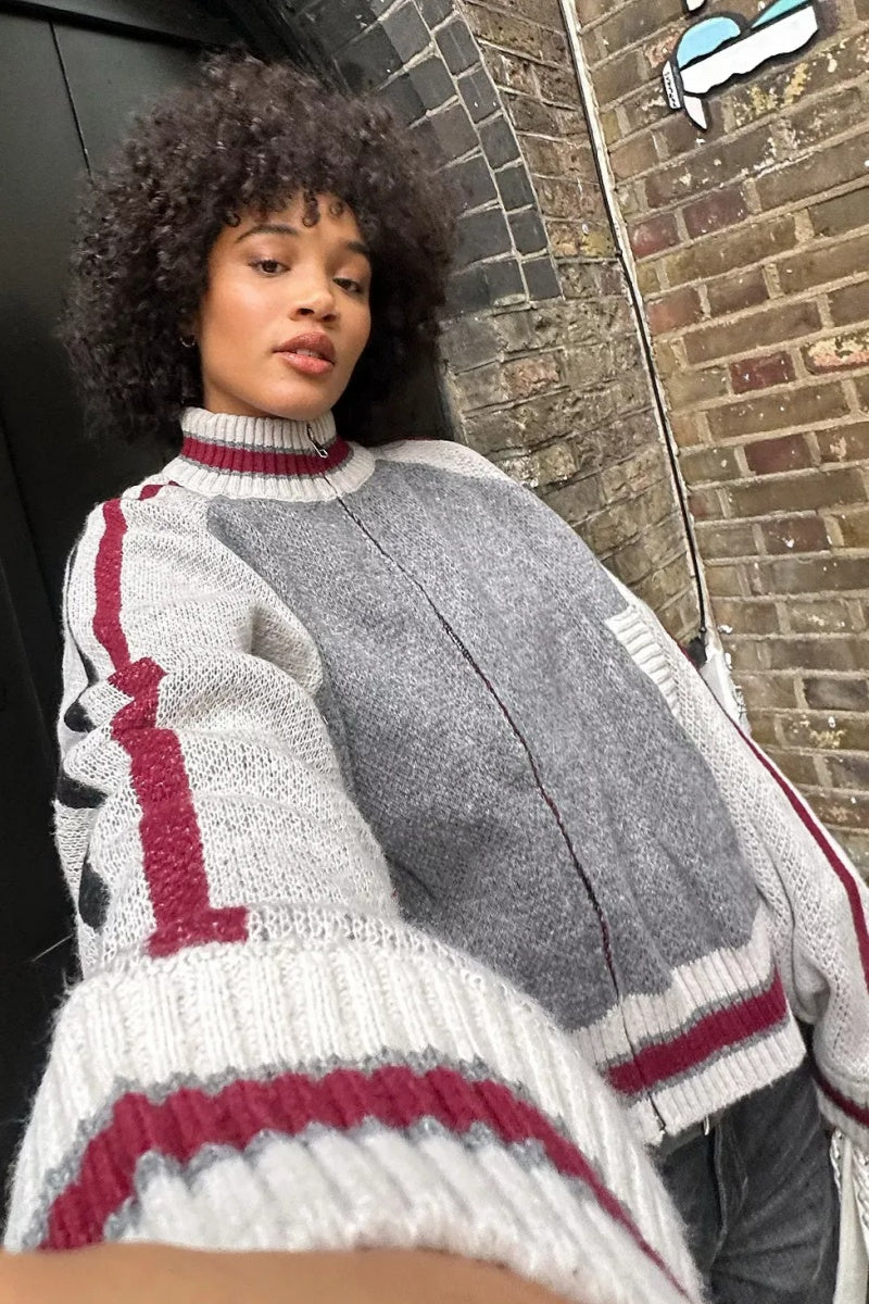 Gray - A model wearing a grey colour block knit bomber jacket with a zip front and sporty striped ribbed trims, paired with blue jeans.