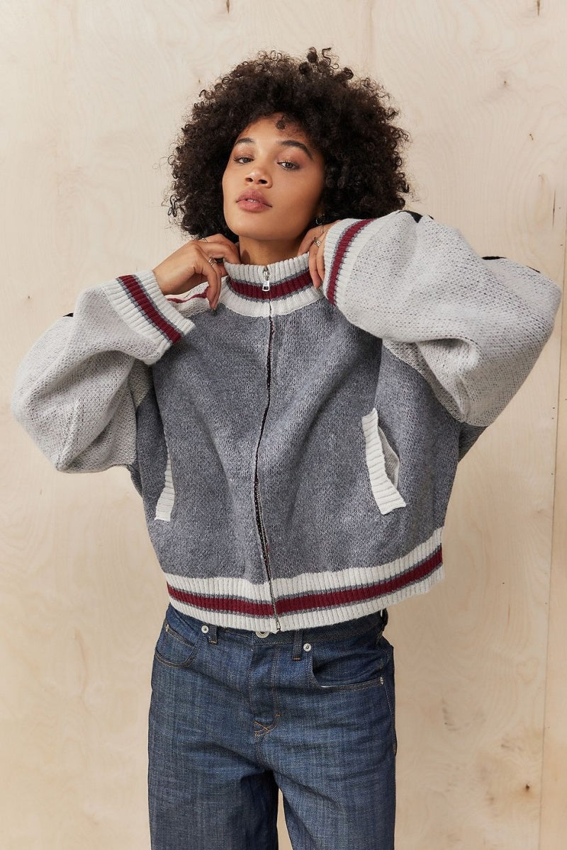 Gray - A model wearing a grey colour block knit bomber jacket with a zip front and sporty striped ribbed trims, paired with blue jeans.