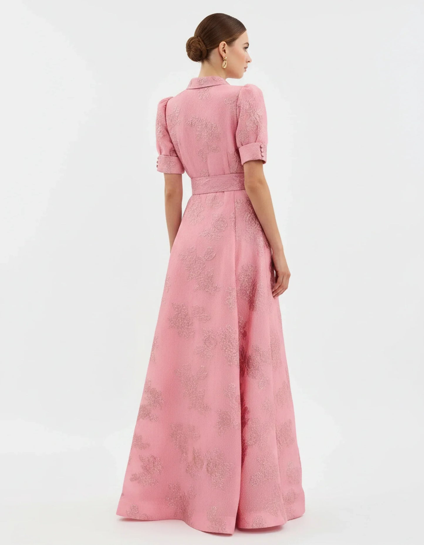 Woman wearing a long heavyweight jacquard maxi dress with a textured floral design, short puff sleeves, collared neckline, button-down front, and matching waist belt
